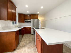 Kitchen featuring appliances with stainless steel finishes, a center island, light countertops, a sink, and recessed lighting