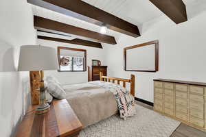 Bedroom featuring beamed ceiling, light wood-style flooring, and baseboards