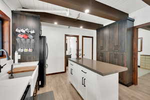 Kitchen with wooden ceiling, a kitchen island, light wood-style floors, white cabinets, and beamed ceiling