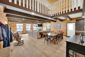 Dining space featuring a stone fireplace, wood walls, light wood-type flooring, and beam ceiling