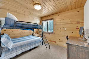 Bedroom with wood ceiling, light carpet, and wooden walls