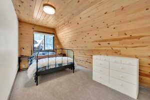 Bedroom featuring lofted ceiling, wood walls, wood ceiling, and light colored carpet