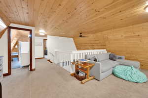 Living area with wood ceiling, wooden walls, carpet flooring, and an upstairs landing