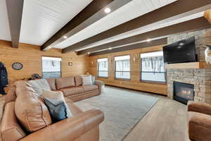 Living area featuring a healthy amount of sunlight, wood walls, beamed ceiling, and a stone fireplace