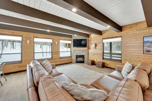 Living area featuring beam ceiling, recessed lighting, light wood-style flooring, wooden walls, and a stone fireplace