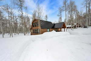 Snow covered property featuring a garage, a standing seam roof, metal roof, and a gambrel roof