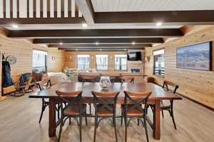 Dining area with a stone fireplace, recessed lighting, wood walls, light wood-type flooring, and beam ceiling