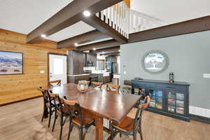 Dining room featuring light wood finished floors, visible vents, beamed ceiling, and wood walls