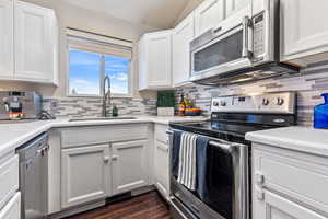 Kitchen featuring decorative backsplash, white cabinetry, solid surface counters,  stainless steel appliances