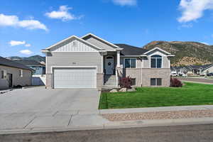 View of front facade with brick siding, concrete driveway, board and batten siding, a front yard, and a mountain view