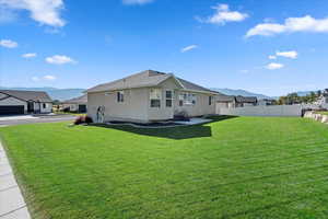 Rear view of house featuring a mountain view, fence, a lawn, a residential view, and stucco siding