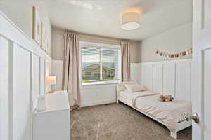 Bedroom featuring light carpet, a wainscoted wall, a decorative wall, and a textured ceiling