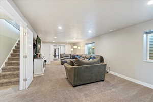 Living room with recessed lighting, light carpet, visible vents, baseboards, and stairway