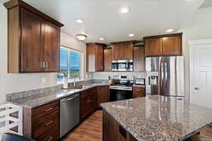 Kitchen featuring stone counters, recessed lighting, appliances with stainless steel finishes, a sink, and a kitchen island