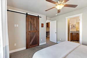 Bedroom featuring a barn door, baseboards, a ceiling fan, ensuite bath, and carpet floors