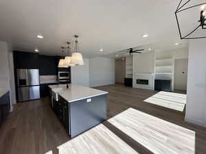 Kitchen featuring a center island with sink, dark cabinetry, decorative light fixtures, and stainless steel fridge with ice dispenser