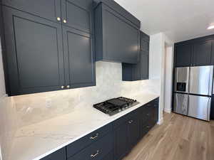 Kitchen with light wood finished floors, stainless steel appliances, backsplash, a textured ceiling, and light stone countertops