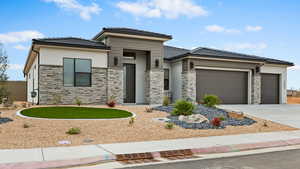 Prairie-style home featuring a tiled roof, an attached garage, stone siding, and driveway