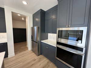 Kitchen with light wood finished floors, decorative backsplash, light stone countertops, stainless steel appliances, and a textured ceiling