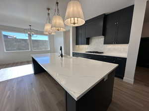 Kitchen featuring a sink, a center island with sink, pendant lighting, and dark cabinetry