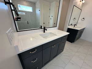 Full bath featuring marble finish floor, a stall shower, two vanities, and a sink