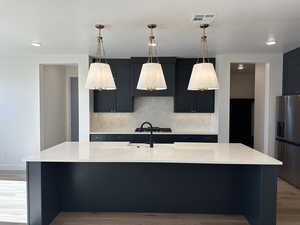 Kitchen with hanging light fixtures, a kitchen island with sink, light stone counters, and stainless steel refrigerator with ice dispenser