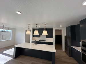 Kitchen featuring a center island with sink, visible vents, light stone counters, decorative light fixtures, and stainless steel appliances