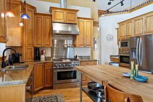 Kitchen featuring stainless steel appliances, hanging light fixtures, a sink, ventilation hood, and dark stone counters