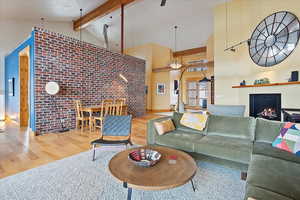 Living room with brick wall, wood finished floors, high vaulted ceiling, beamed ceiling, and a lit fireplace