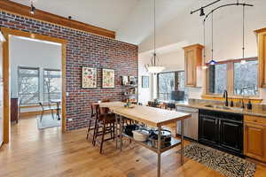 Kitchen featuring decorative light fixtures, light wood-style floors, a sink, brick wall, and dishwasher