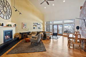 Living room featuring a ceiling fan, a glass covered fireplace, light wood-style flooring, and a high ceiling