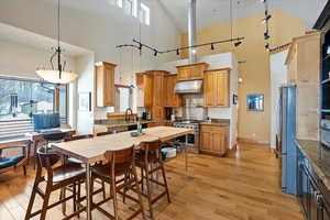 Kitchen with light wood finished floors, hanging light fixtures, appliances with stainless steel finishes, and under cabinet range hood