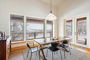 Dining area with light wood-type flooring, high vaulted ceiling, and french doors