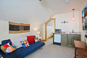 Living area featuring light carpet, a toaster, baseboards, vaulted ceiling, and a textured ceiling