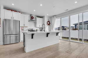 Kitchen featuring stainless steel appliances, light countertops, a center island with sink, and wall chimney exhaust hood