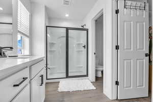 Bathroom with visible vents, toilet, a stall shower, vanity, and wood finished floors