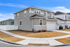 View of front of house with a garage, fence, stone siding, concrete driveway, and stucco siding