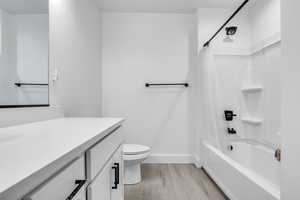 Bathroom with toilet, shower / tub combo, vanity, wood finished floors, and baseboards