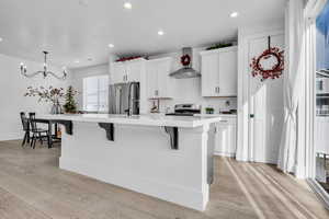 Kitchen with wall chimney exhaust hood, a spacious island, and light countertops