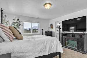 Bedroom with a textured ceiling, light carpet, a glass covered fireplace, and ensuite bathroom