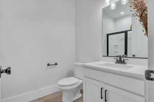 Full bathroom featuring a shower, toilet, vanity, wood finished floors, and baseboards