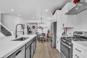 Kitchen with light countertops, wall chimney range hood, a sink, and appliances with stainless steel finishes