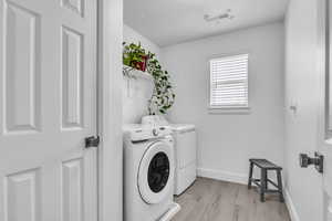 Clothes washing area with laundry area, light wood finished floors, visible vents, baseboards, and separate washer and dryer