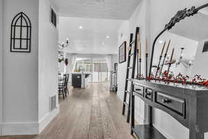 Corridor with a textured ceiling, light wood-style flooring, visible vents, and baseboards