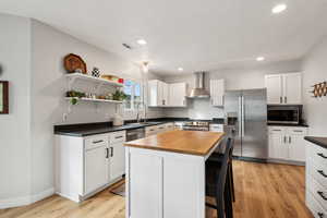 Kitchen featuring wall chimney exhaust hood, appliances with stainless steel finishes, a kitchen island, and white cabinets