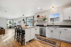 Kitchen featuring dishwasher, a sink, white cabinetry, and decorative light fixtures