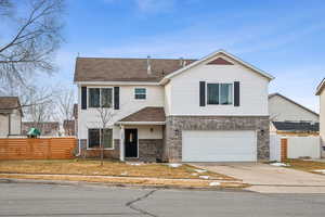 View of front facade with a garage, driveway, brick siding, and fence