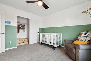 Bedroom featuring a crib, baseboards, ceiling fan, carpet floors, and a closet