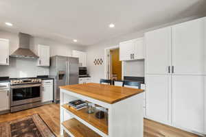 Kitchen with light wood-style floors, wall chimney exhaust hood, appliances with stainless steel finishes, and white cabinets