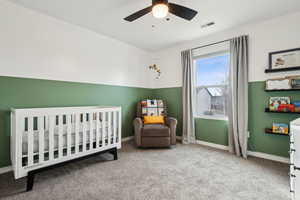 Carpeted bedroom featuring a nursery area, baseboards, visible vents, and ceiling fan